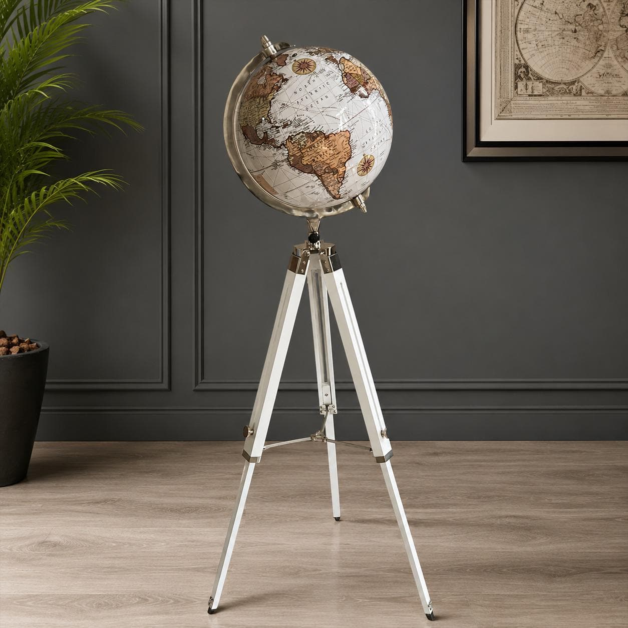 Vintage cream world globe with a metal meridian ring on a tall white and chrome tripod floor stand beside a dark panelled wall