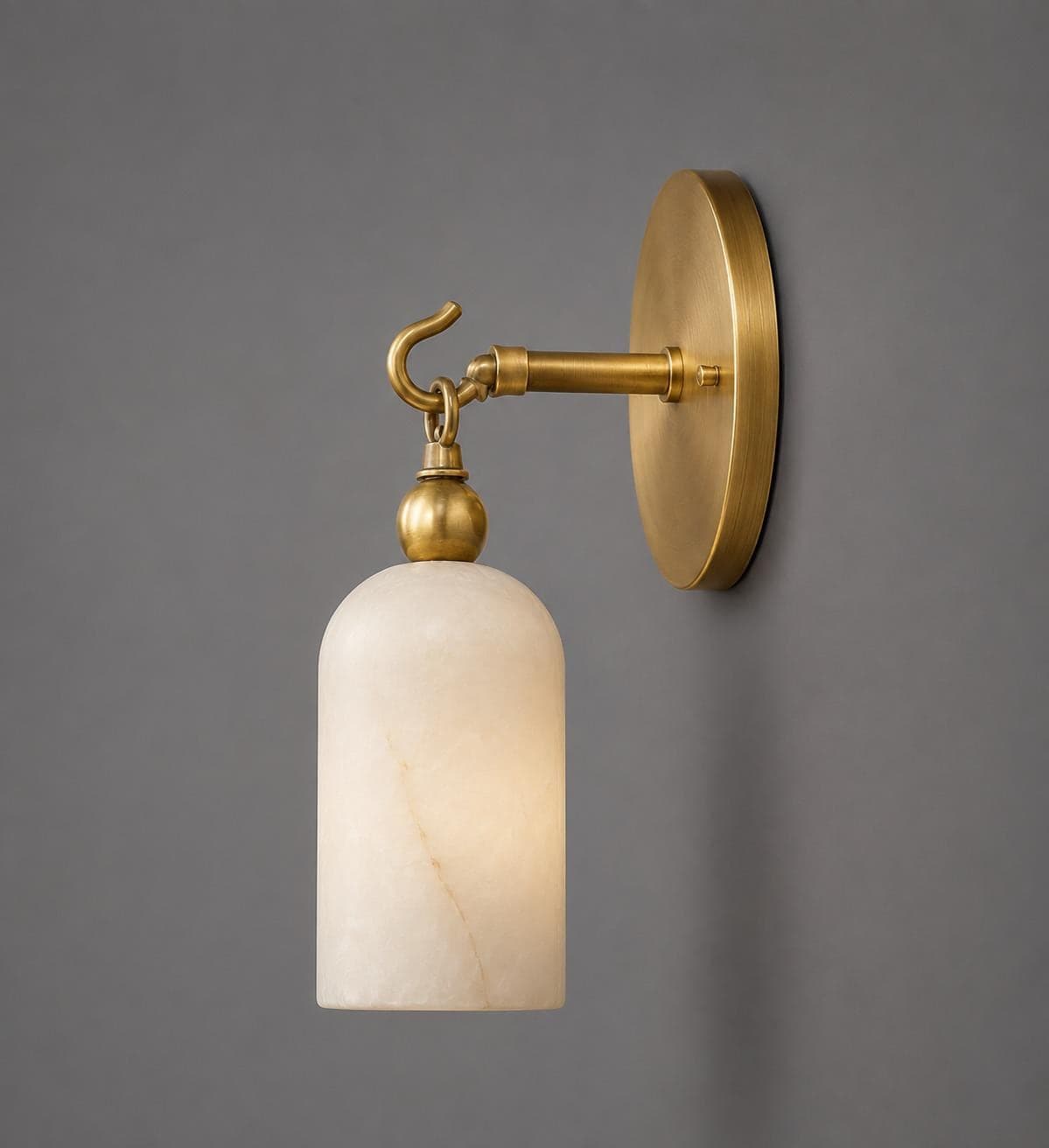 Wall sconce with a cylindrical veined alabaster shade hanging from a brass ball and open hook on a large round brass backplate