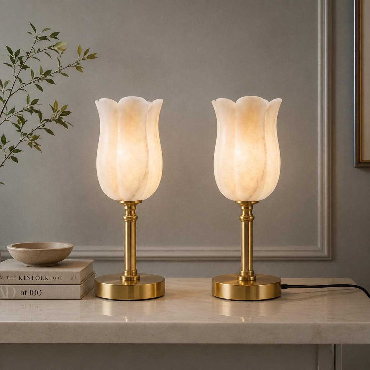 Pair of alabaster tulip table lamps lit on a marble console beside a framed print